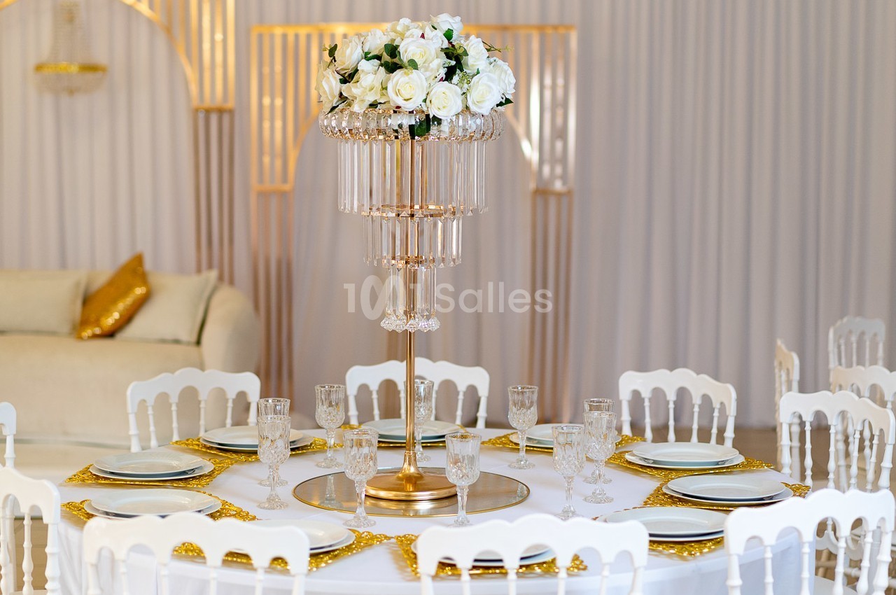 Centre de table doré avec fleurs blanches et pampilles, entouré d'assiettes et de verres sur une table élégante.