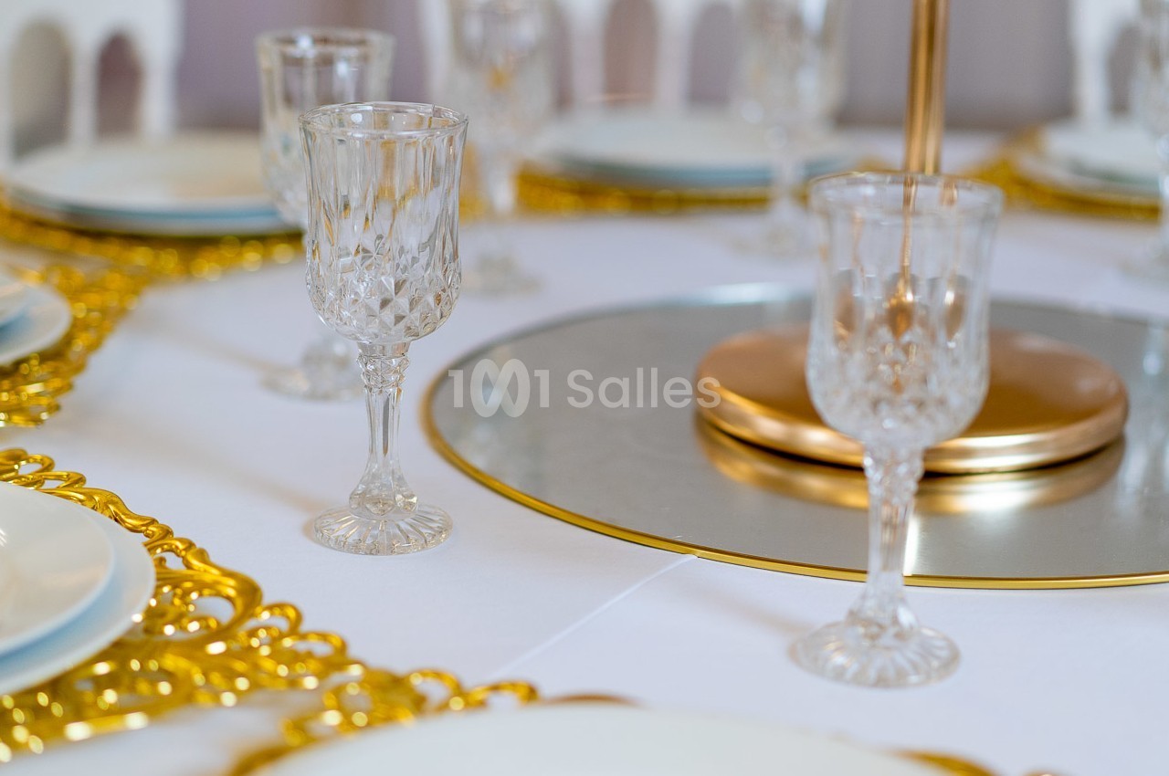 Table dressée avec des verres en cristal, assiettes blanches et détails dorés sur un centre de table élégant.