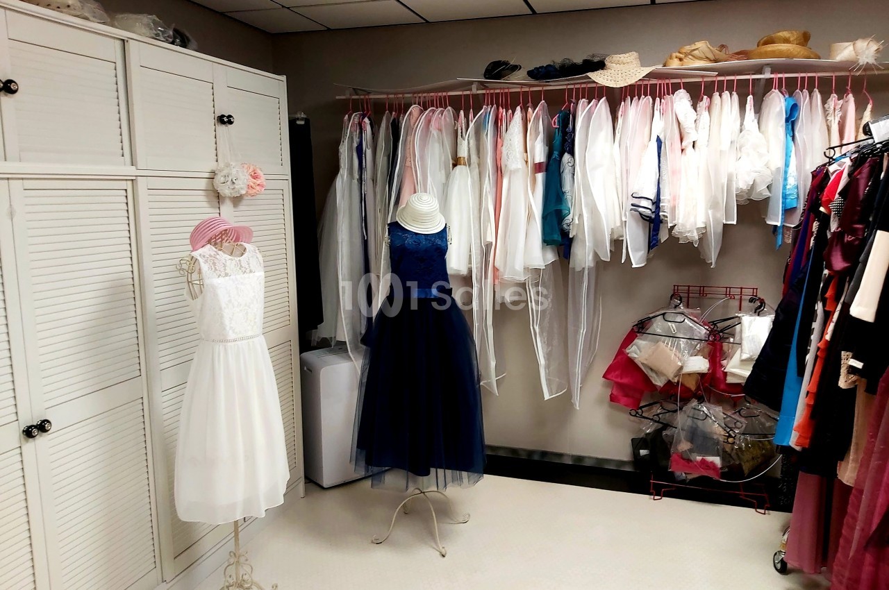 Robes élégantes sur mannequins et vêtements suspendus dans une pièce lumineuse avec rangements et cintres.