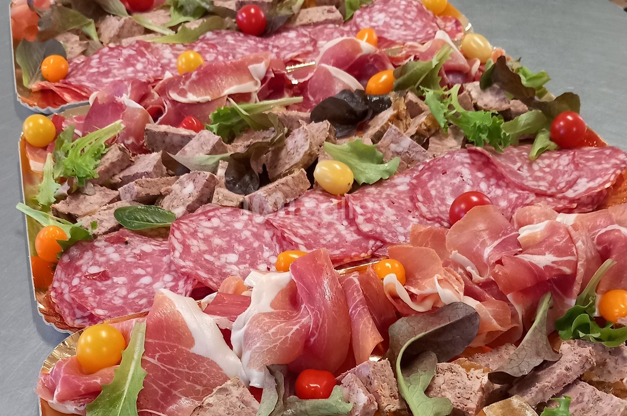 Plateaux garnis de charcuteries variées, feuilles de salade et tomates cerises colorées sur une table en inox.