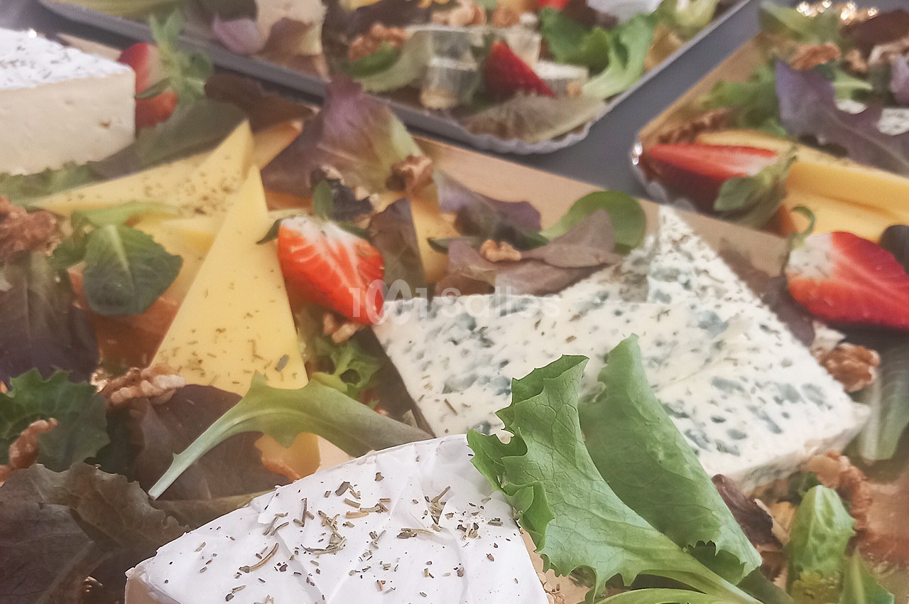 Plateau de fromages variés avec feuilles de salade, noix et morceaux de fraises.