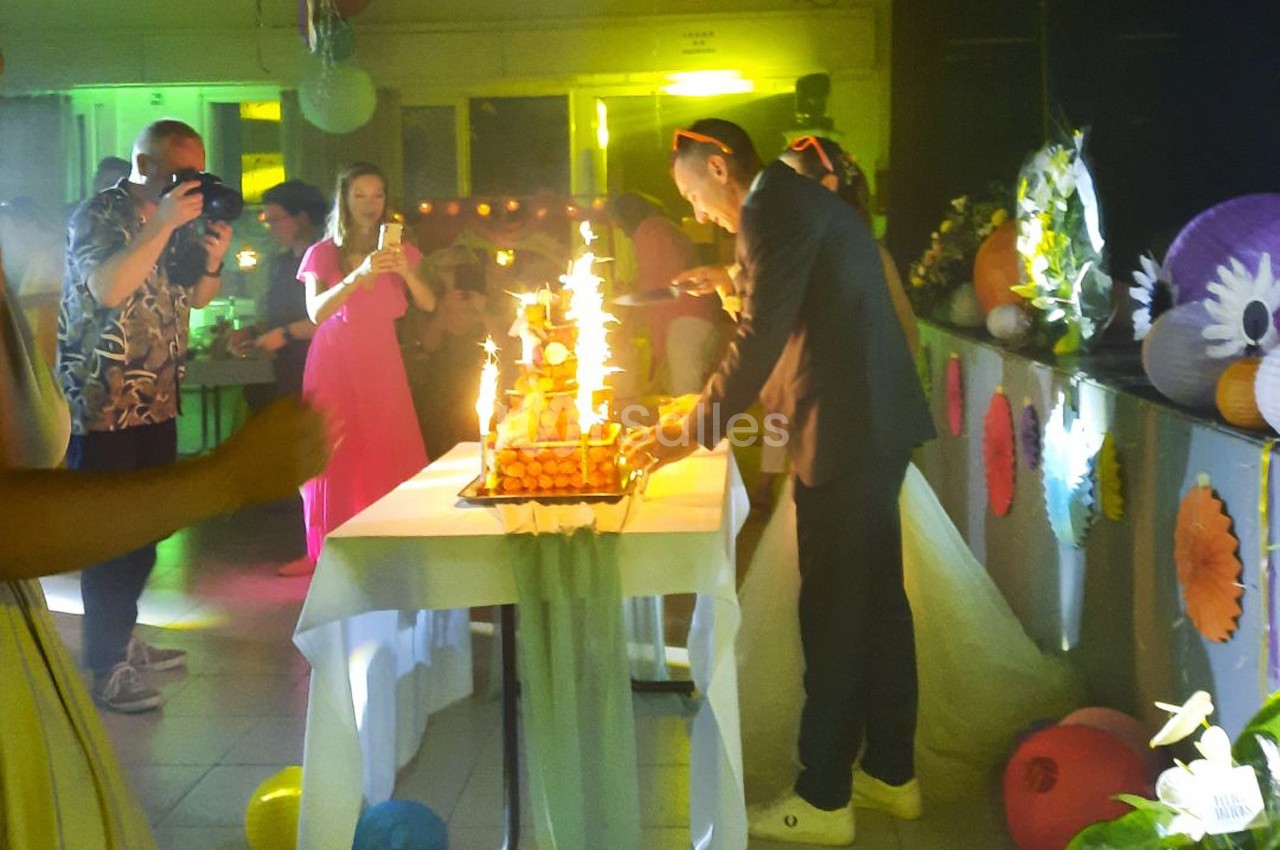 Un couple coupe un gâteau éclairé de bougies étincelantes lors d'une fête dans une salle décorée.