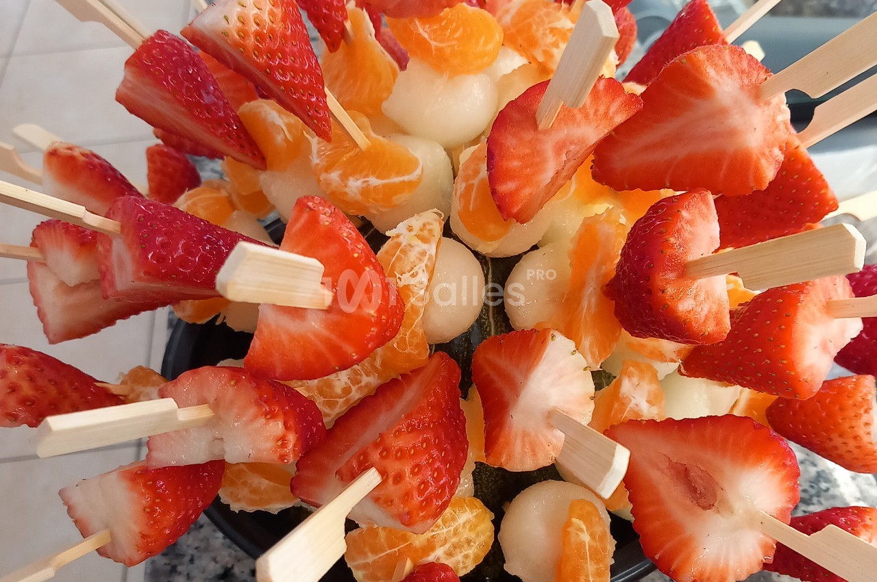 Brochettes de fruits composées de fraises, quartiers de mandarine et billes de melon disposées en bouquet.