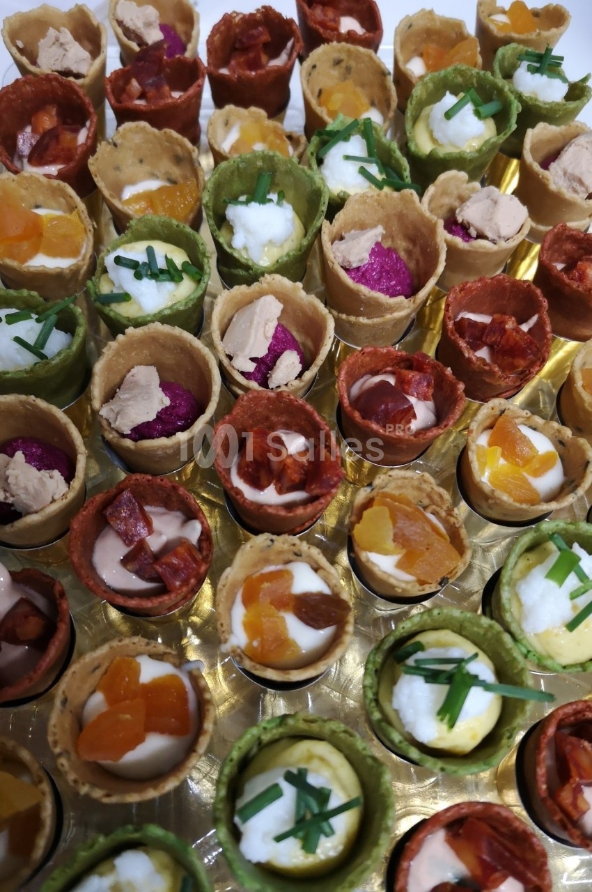 Assortiment de mini-cornets colorés garnis de mousse, légumes, fromage et herbes fraîches, présenté sur un plateau.