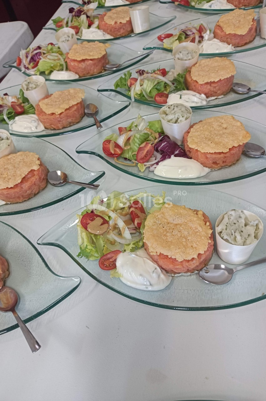 Assiettes de tartares de saumon avec salade, sauces et cuillères, présentées sur des plats en verre.