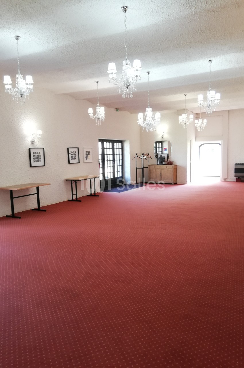 Salle spacieuse avec moquette rouge, murs blancs, lustres suspendus et mobilier minimaliste.