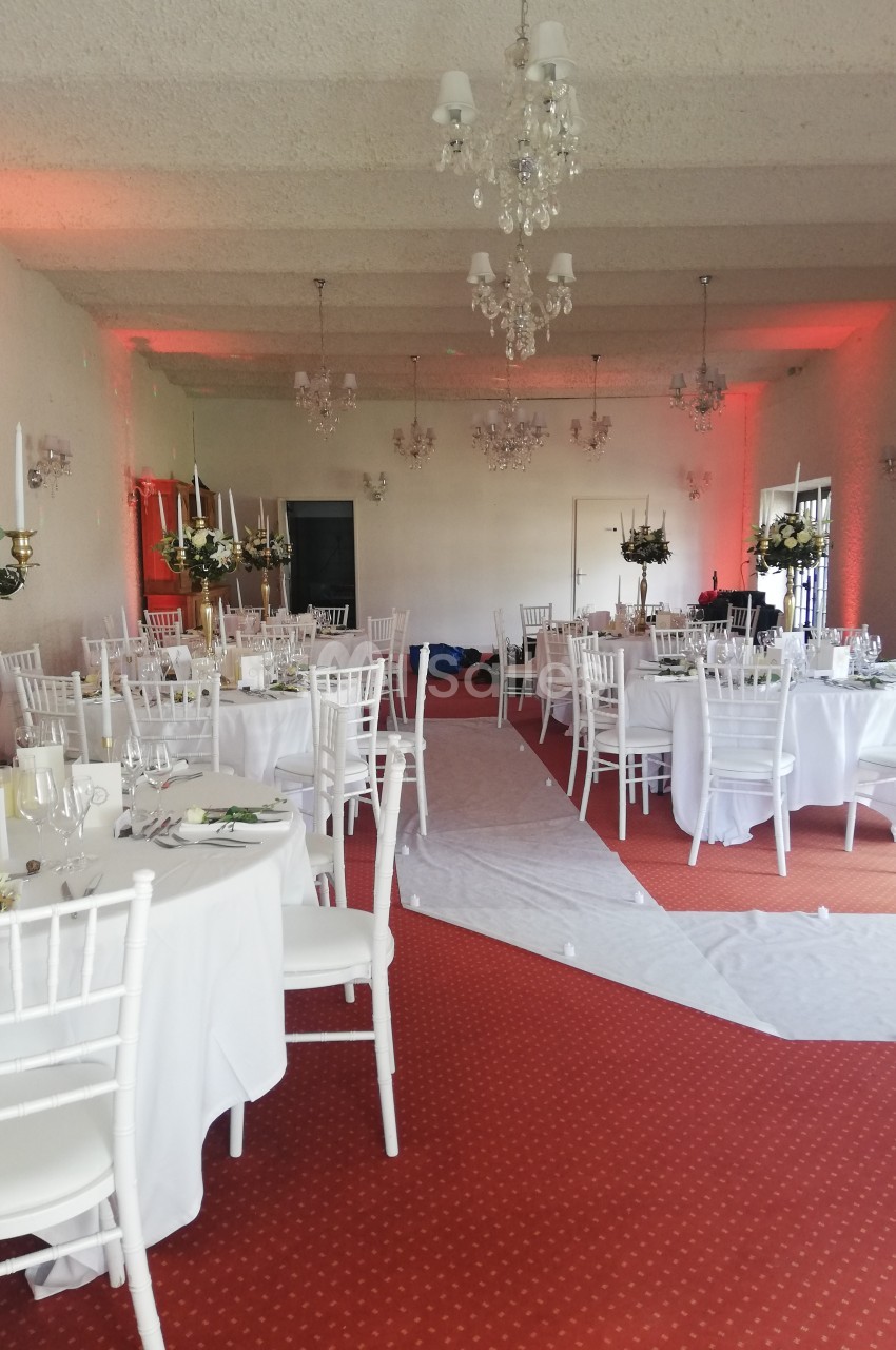 Salle de réception décorée avec des tables rondes, chaises blanches et centres de table fleuris.