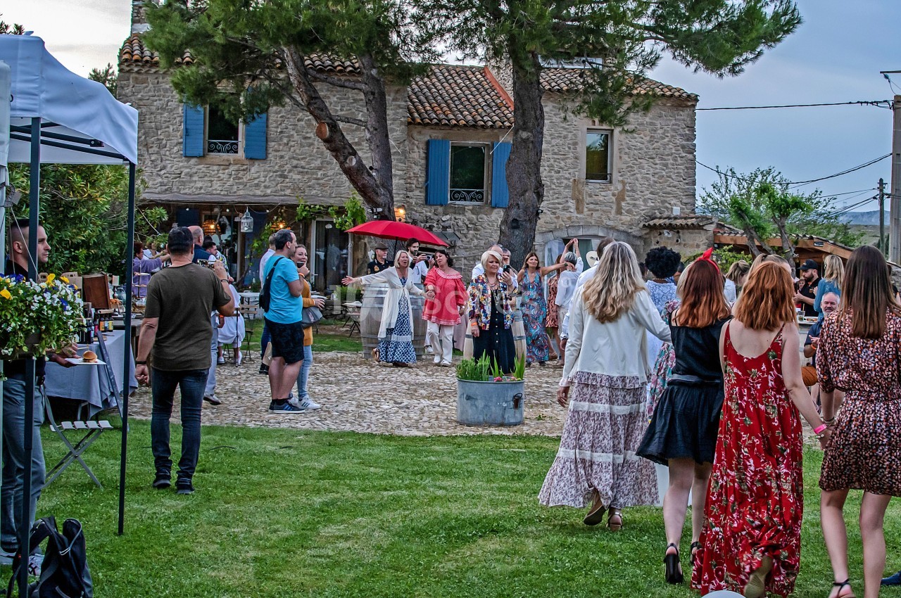 Groupe de personnes rassemblées dans un jardin devant une maison en pierre, lors d'un événement en plein air.