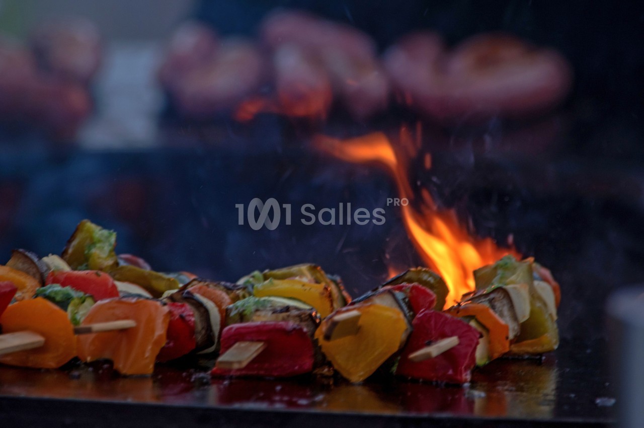 Brochettes de légumes colorés grillant sur une plaque chaude avec des flammes en arrière-plan.