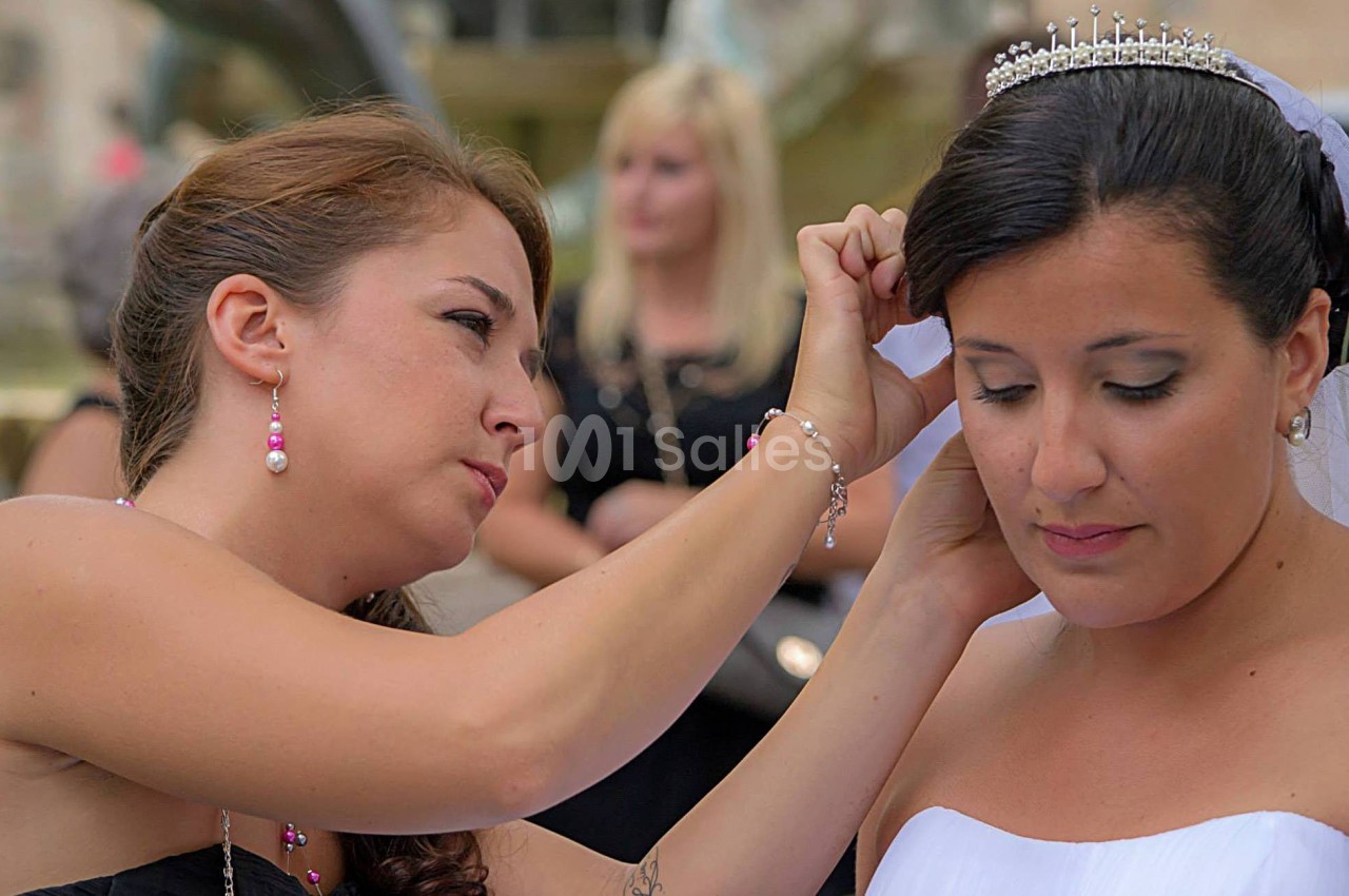 Une femme ajuste le voile ou la coiffure d'une mariée portant une robe blanche et un diadème.