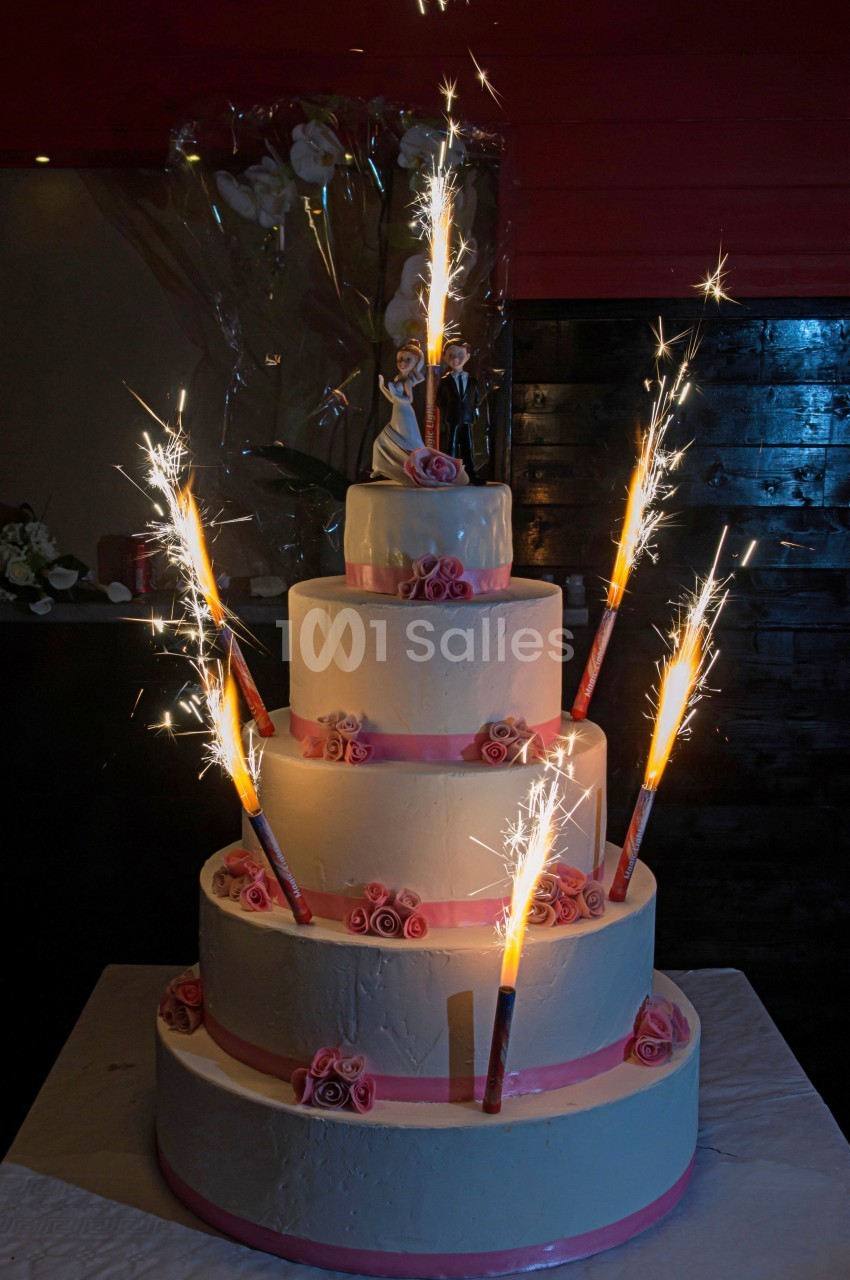 Gâteau de mariage à quatre étages décoré de roses roses et de cierges magiques allumés.