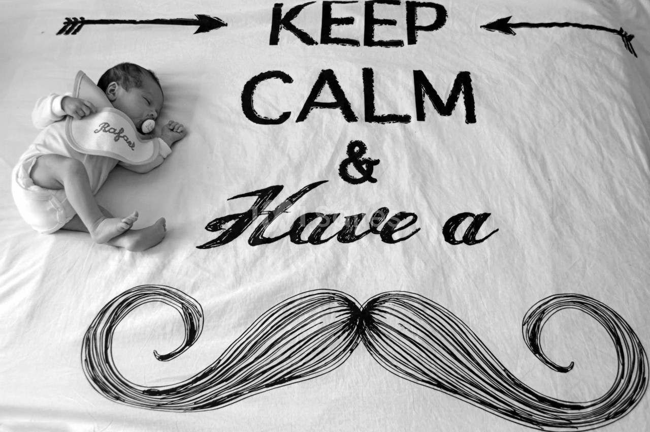 Nouveau-né dormant sur une couverture avec l'inscription ’Keep Calm & Have a’ et un dessin de moustache.