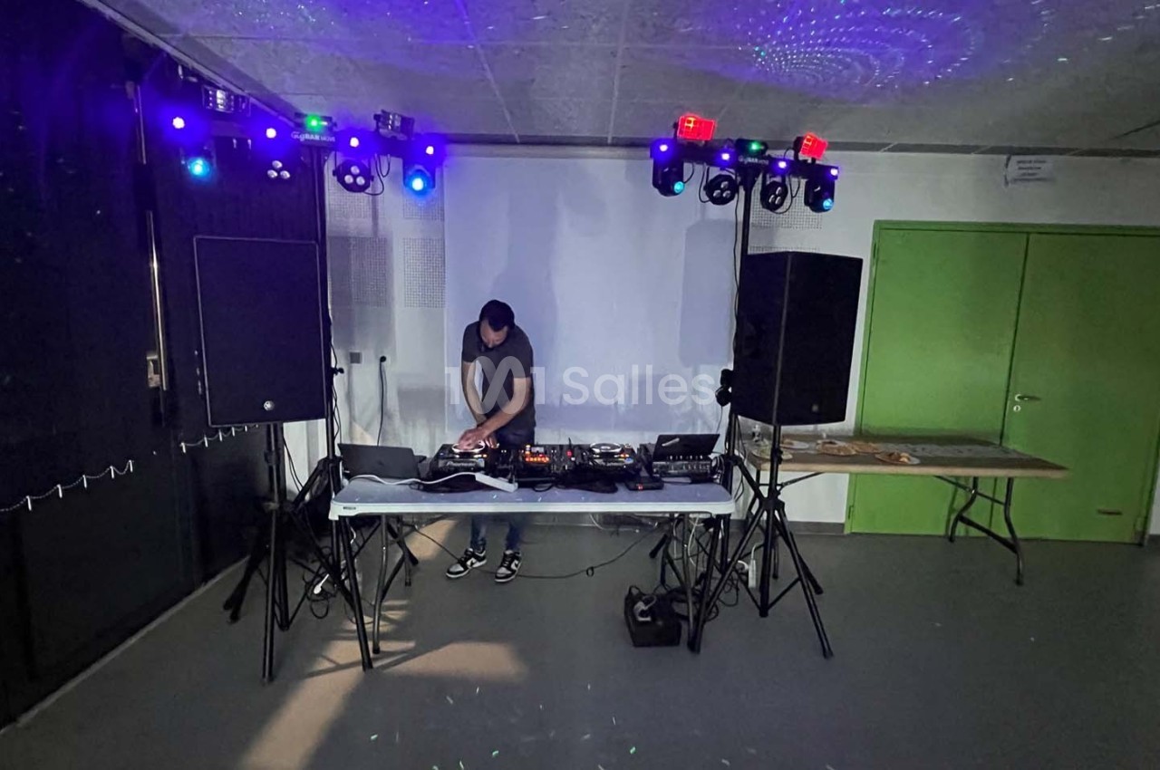 Un DJ mixe sur une table équipée de matériel audio, entouré de lumières colorées dans une salle sombre.
