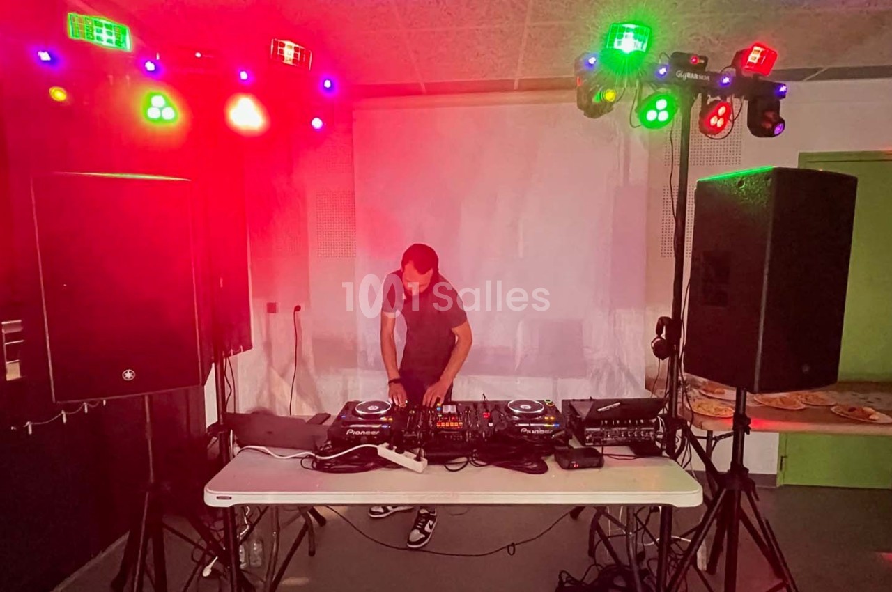 Un DJ mixe sur une table équipée de matériel audio, entouré de lumières colorées dans une salle sombre.