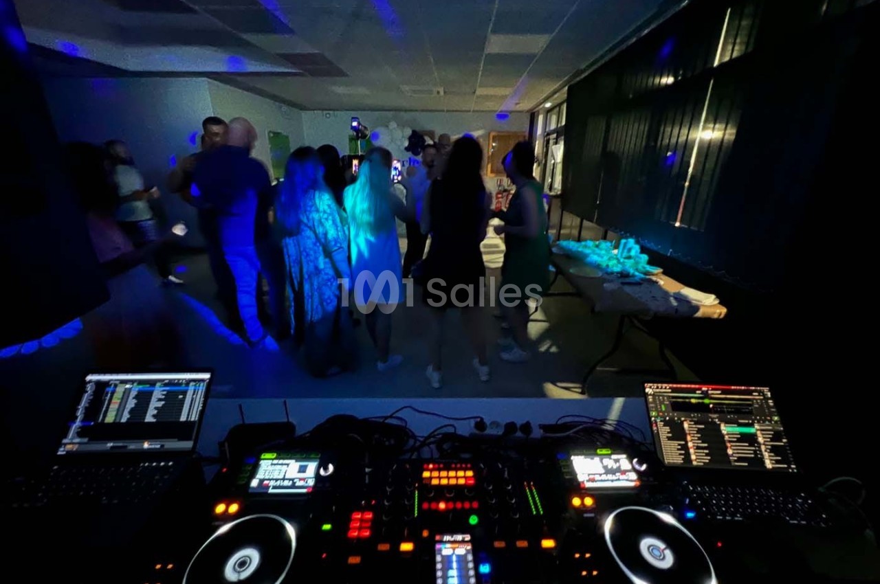 Vue depuis une table de mixage DJ avec des invités dansant dans une salle faiblement éclairée.