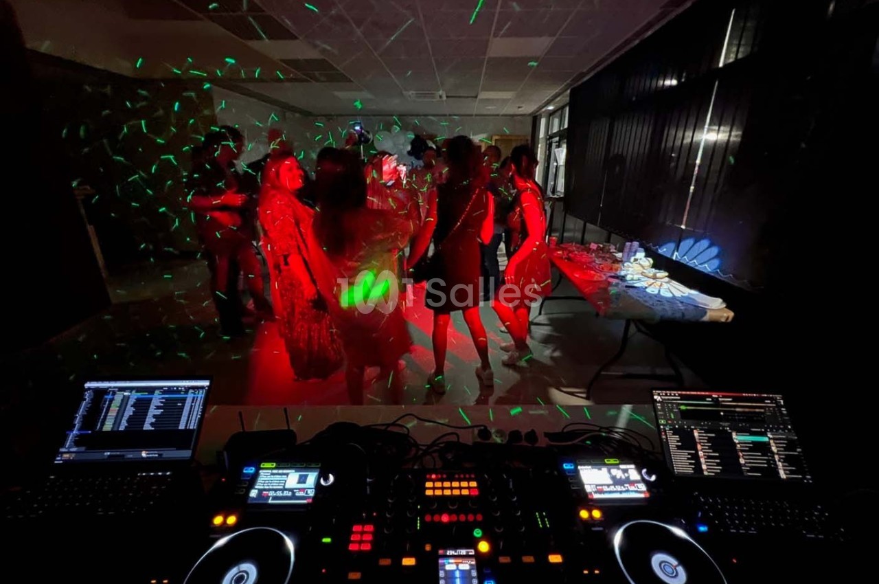 Vue d'une piste de danse sombre éclairée par des lumières colorées, avec des personnes dansant devant une table de mixage.