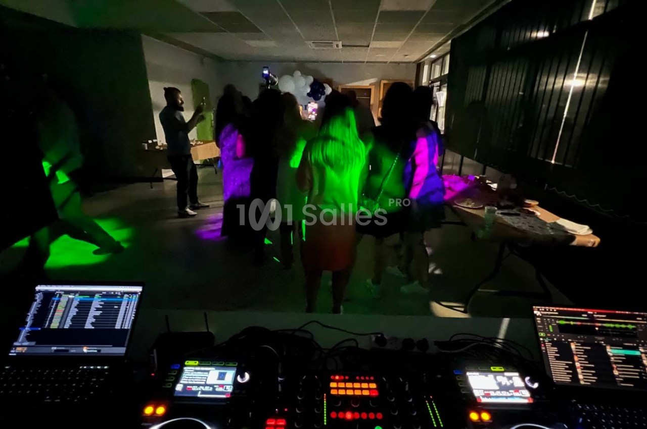 Des personnes dansent dans une salle sombre éclairée par des lumières colorées, avec une table de mixage au premier plan.