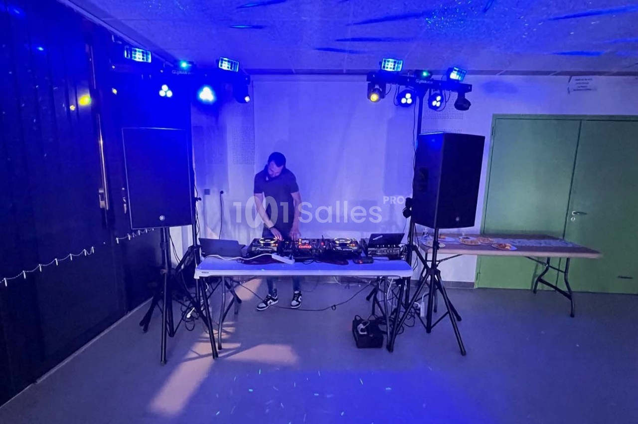 Un DJ mixe sur une table équipée de matériel audio, entouré de haut-parleurs et éclairé par des lumières colorées.