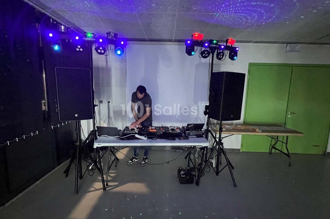 Un DJ mixe sur une table équipée de matériel audio, entouré de lumières colorées dans une salle sombre.