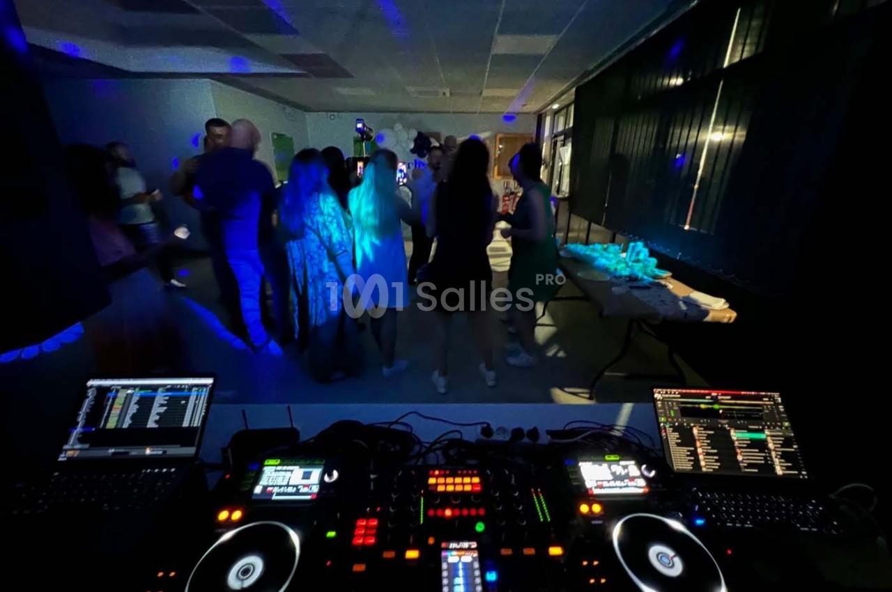 Vue depuis une table de mixage DJ avec des invités dansant dans une salle faiblement éclairée.