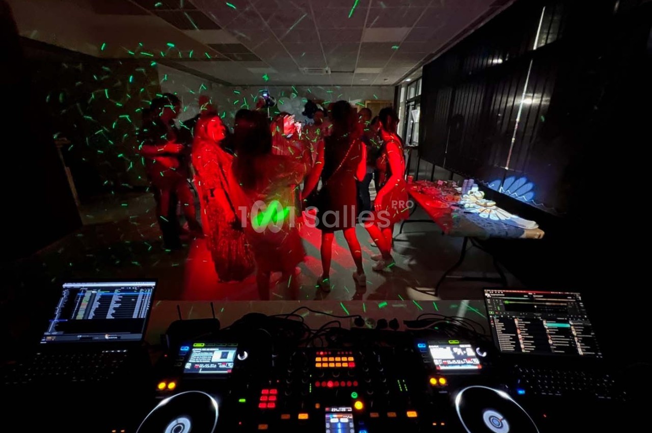 Vue d'une piste de danse sombre éclairée par des lumières colorées, avec des personnes dansant devant une table de mixage.