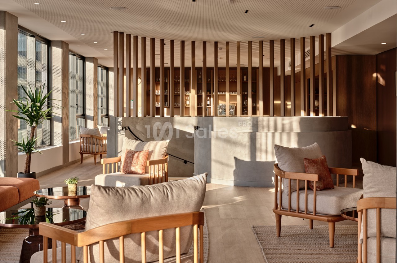 Espace lumineux avec fauteuils en bois, tables basses et parois vitrées, offrant une ambiance chaleureuse et moderne.