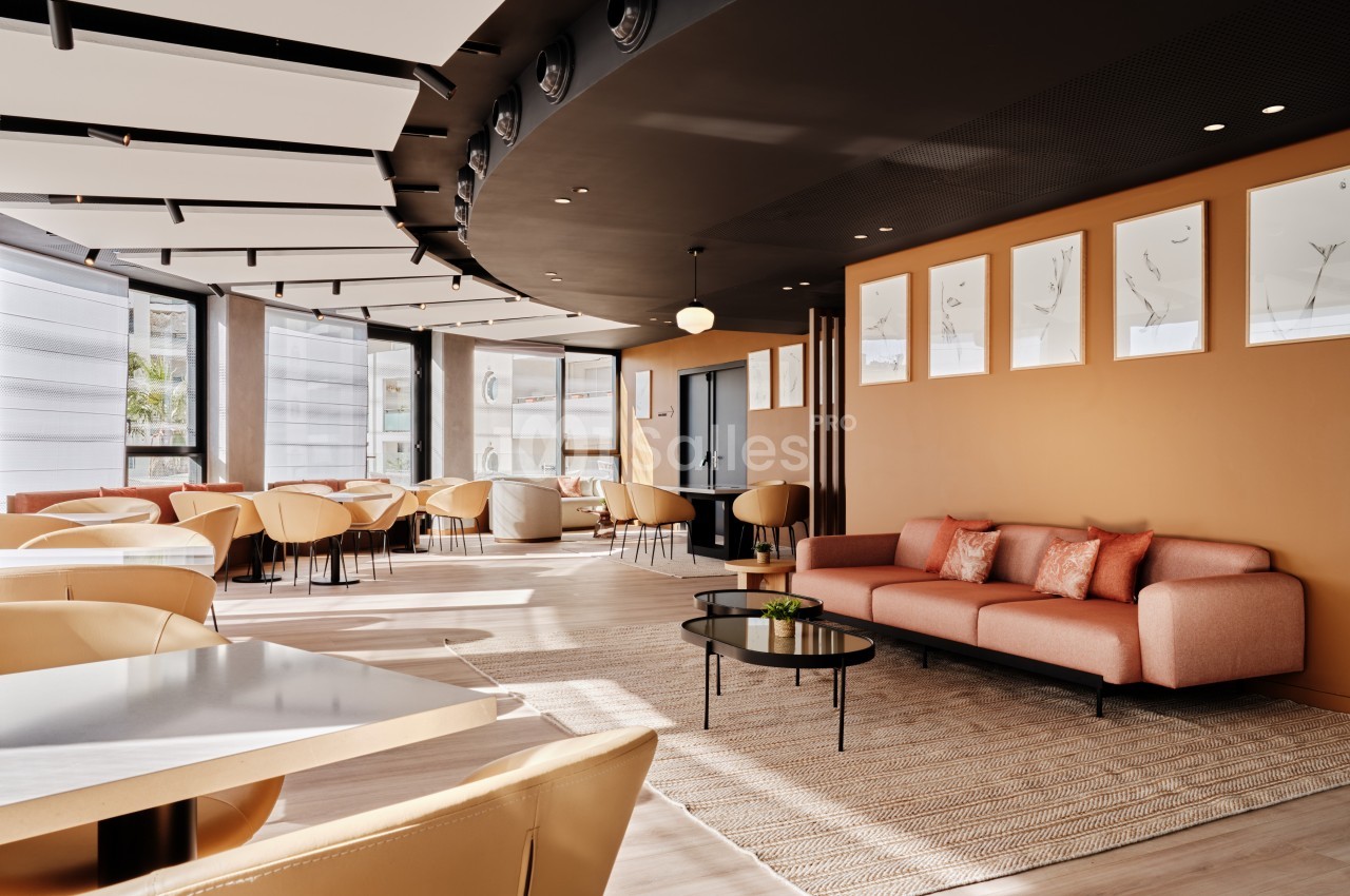 Salle lumineuse avec mobilier moderne, comprenant des tables, des chaises beige clair et un canapé rose sur un tapis.