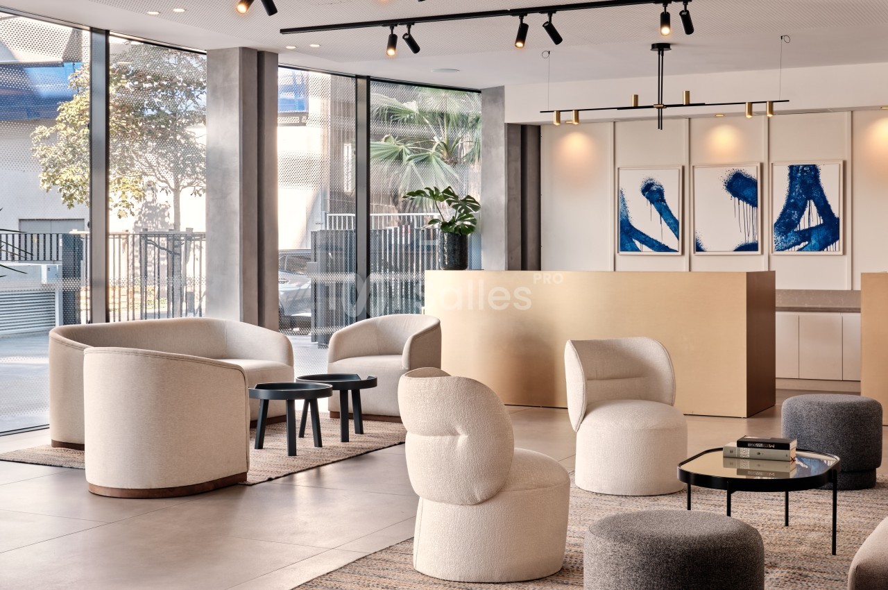 Espace lumineux avec fauteuils modernes, tables basses et comptoir beige, décoré de tableaux abstraits bleus.