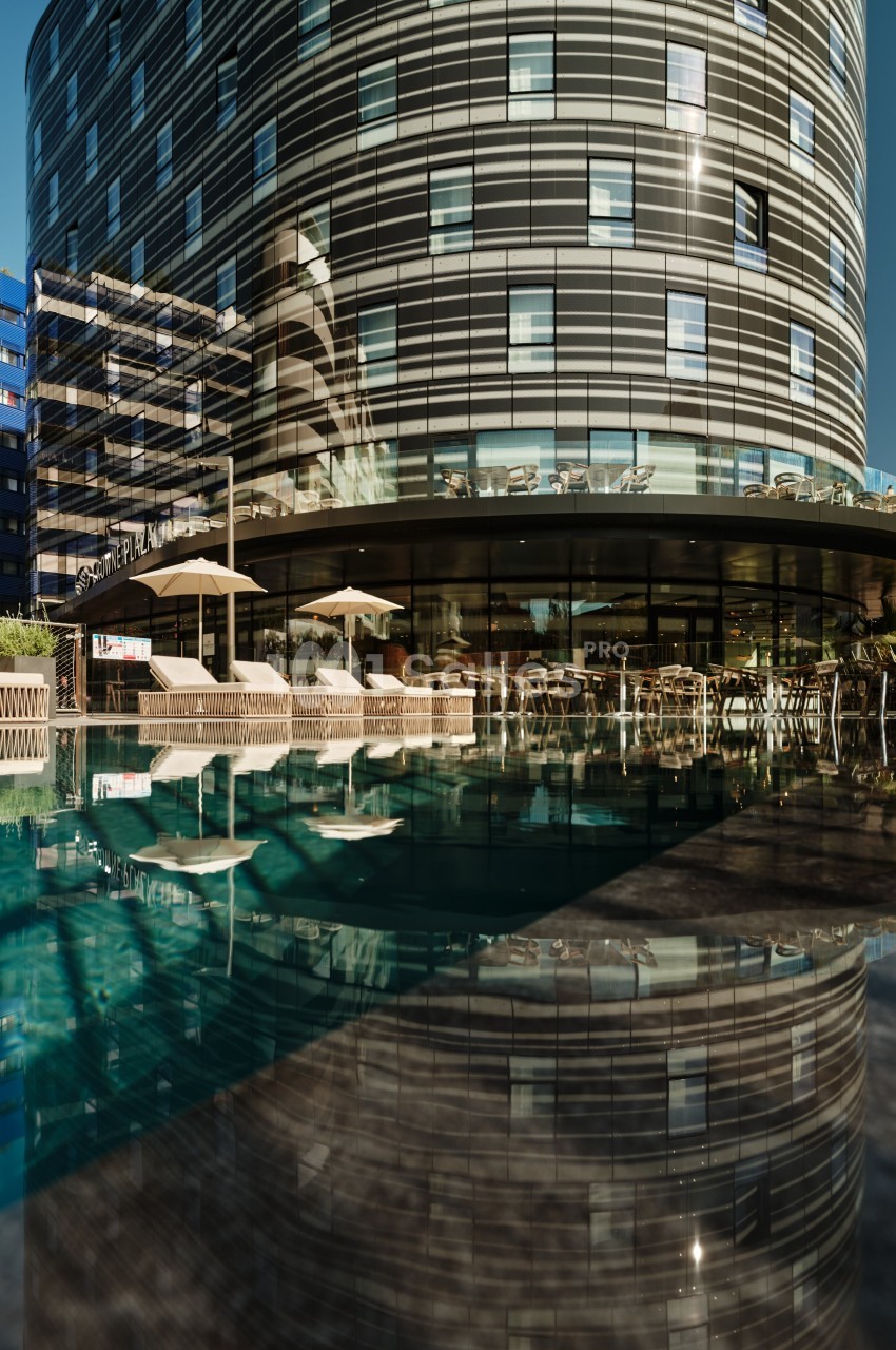 Façade d'un bâtiment moderne avec des baies vitrées, reflétée dans une piscine au premier plan.