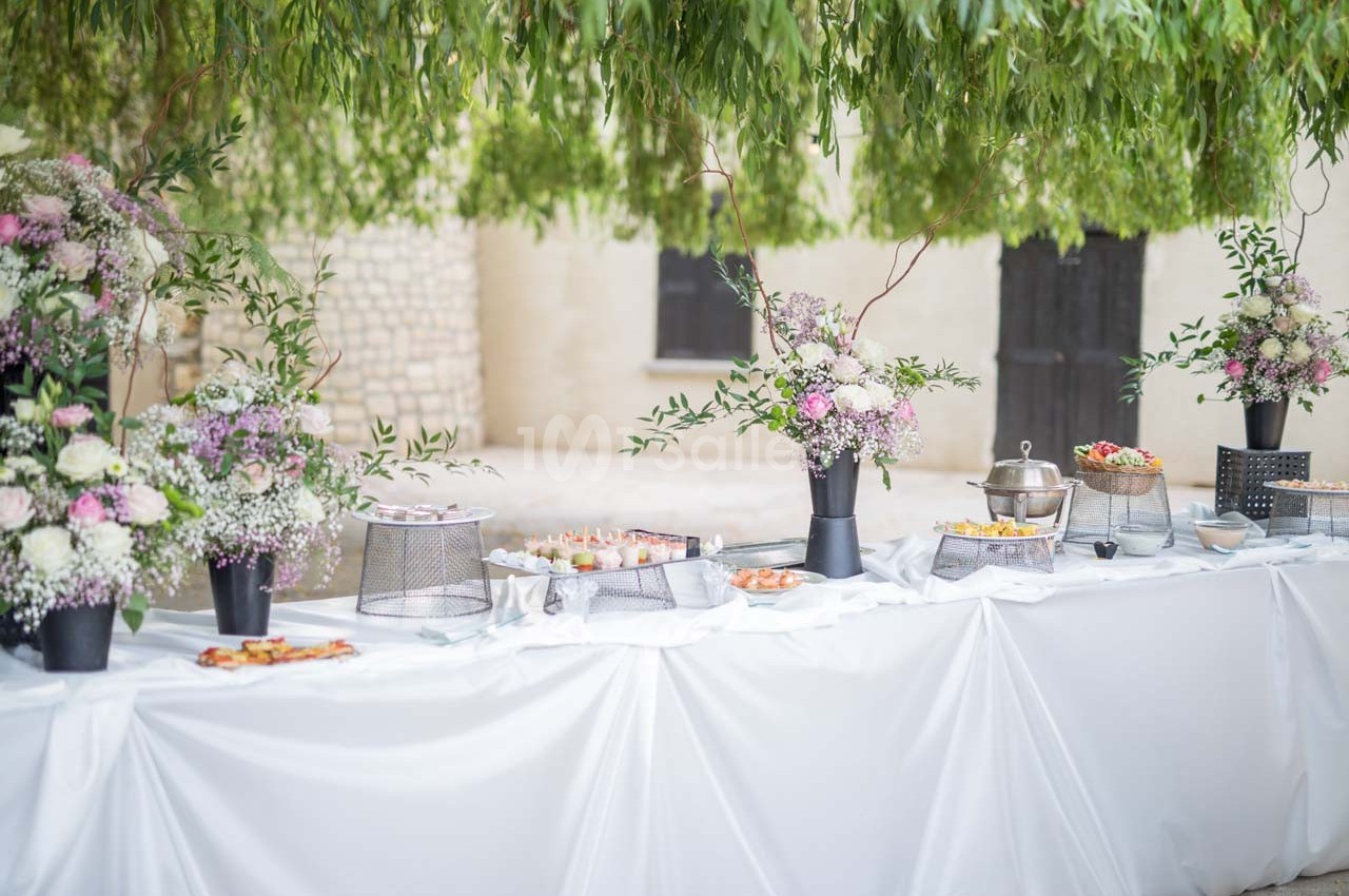 Table de buffet décorée de fleurs et plats variés, installée en extérieur sous des branches d'arbres.