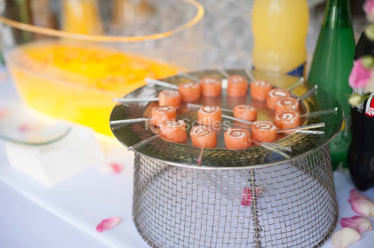 Plateau de bouchées roulées au saumon disposées en cercle sur une grille, entouré de boissons et de décorations.