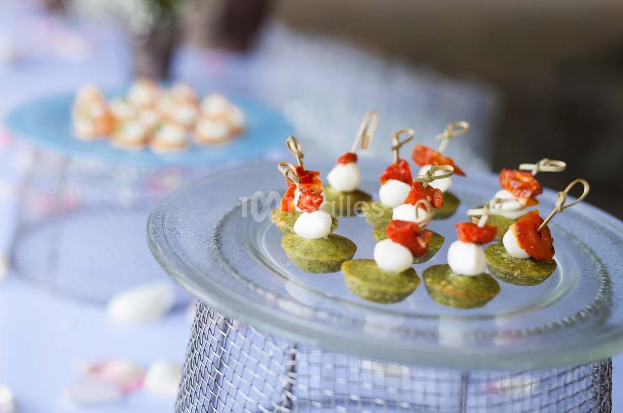 Assortiment de bouchées apéritives avec tomates, mozzarella et base verte, présentées sur un plateau en verre.