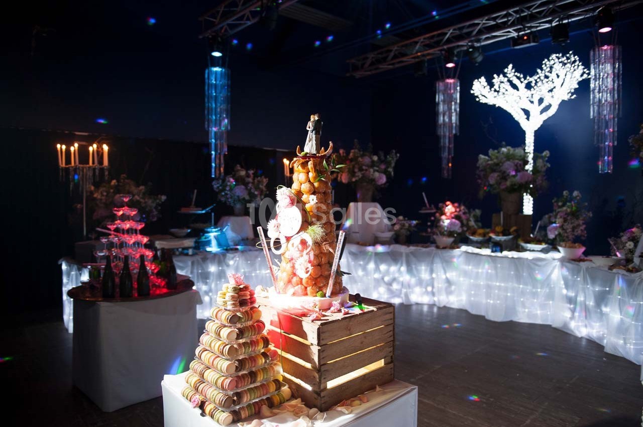 Dessert de fête avec une pièce montée, une pyramide de macarons et une décoration lumineuse dans une salle sombre.