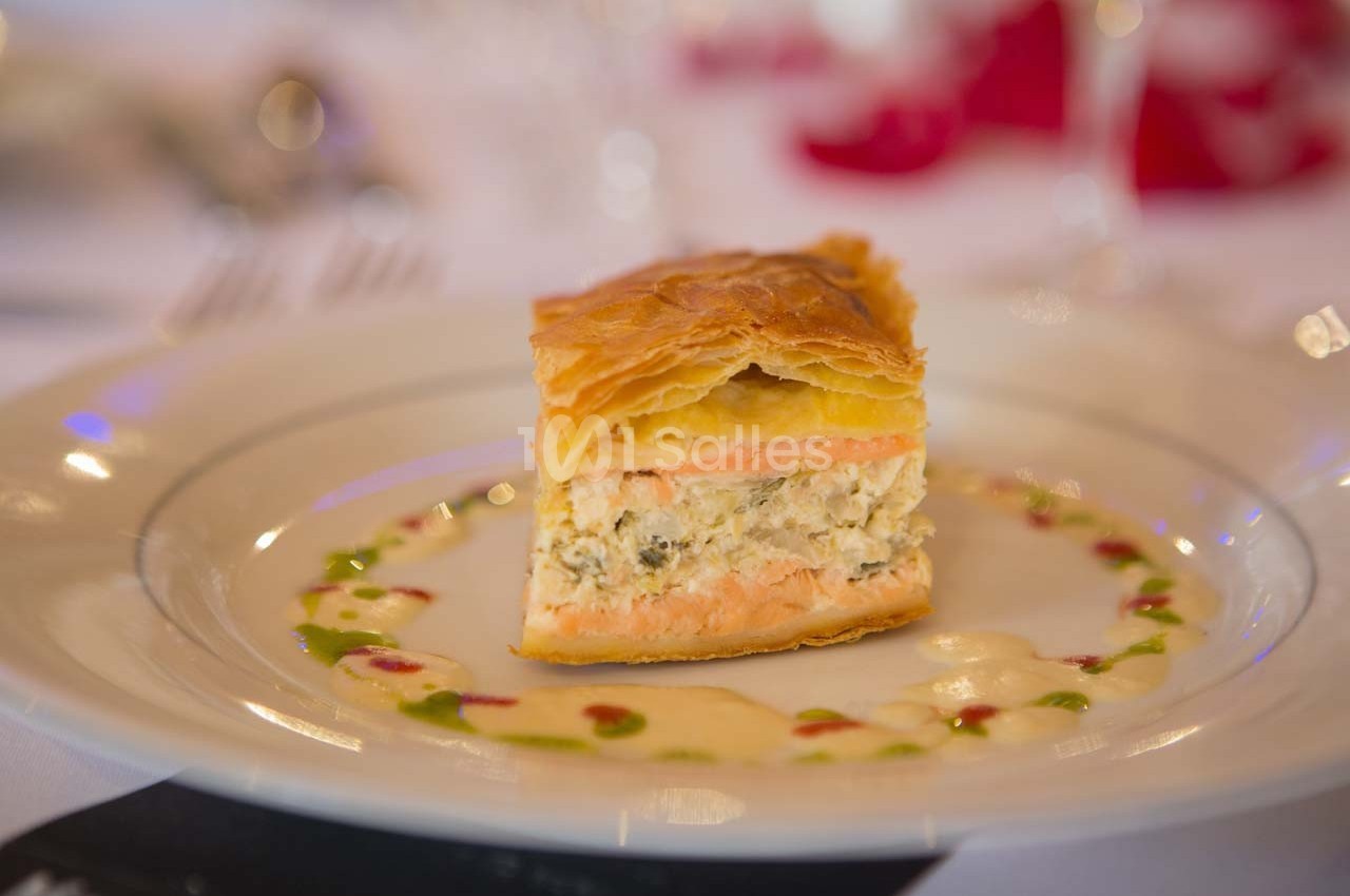 Part de feuilleté au saumon et farce crémeuse, servie sur une assiette avec une sauce décorative colorée.