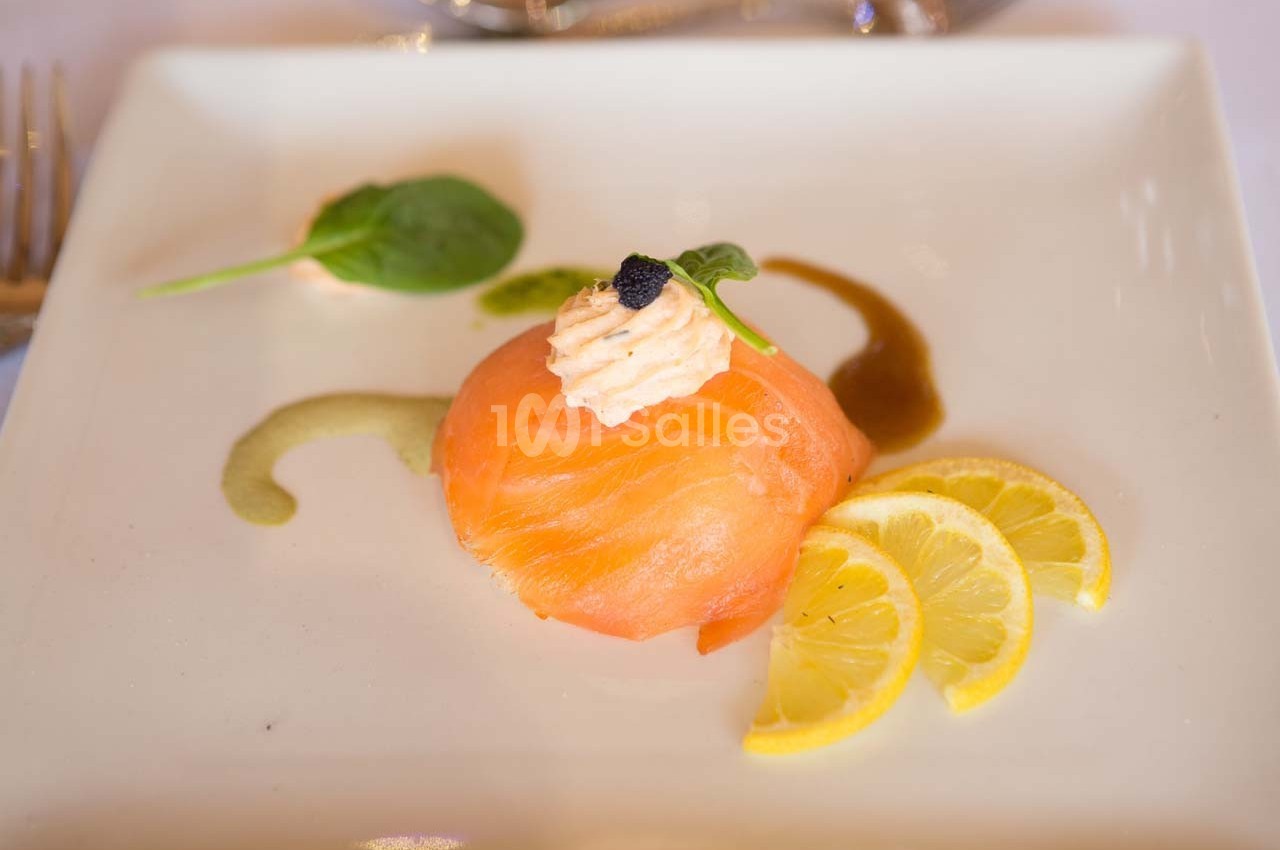 Tranche de saumon fumé garnie de crème et caviar, accompagnée de rondelles de citron et d'épinard sur une assiette blanche.