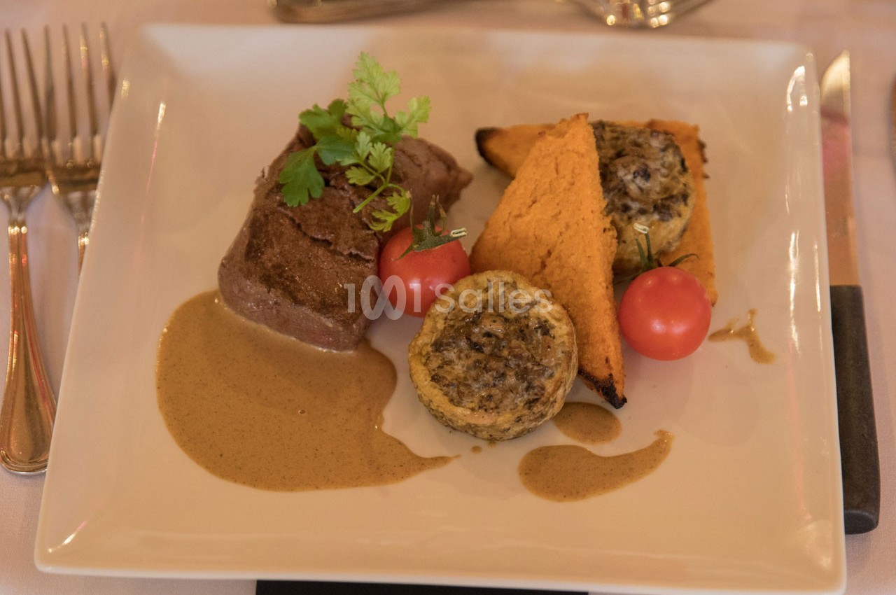 Assiette composée d'un filet de viande, sauce, légumes grillés, tomates cerises et garniture aux champignons.