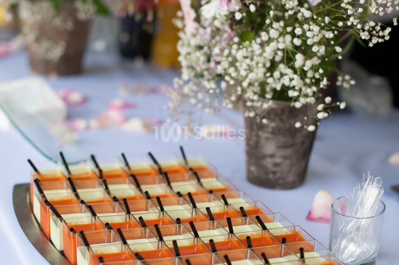 Plateau de verrines colorées alignées sur une table décorée de fleurs et de pétales.