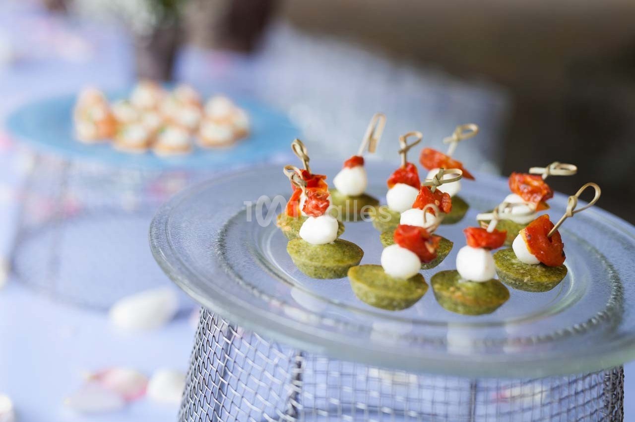 Assiette de bouchées apéritives avec tomates, fromage et base verte, présentées sur une table de réception.
