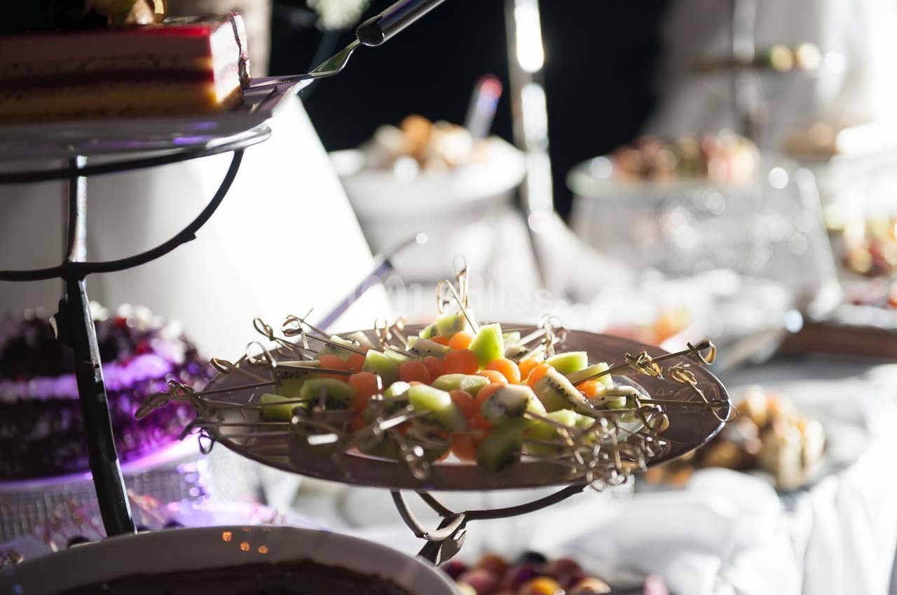 Plateau de fruits frais coupés en morceaux, présenté sur une table de buffet avec d'autres plats en arrière-plan.