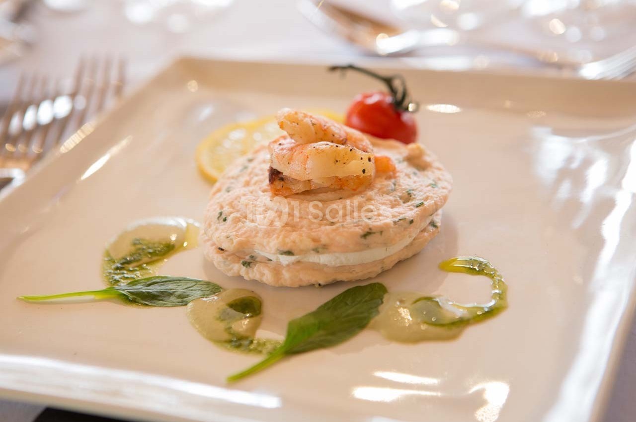 Plat gastronomique composé d'une mousse de poisson garnie de crevettes, tomate cerise et sauce verte décorative.