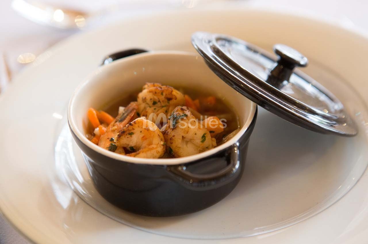 Crevettes sautées servies dans une petite cocotte noire avec des légumes, posée sur une assiette blanche.