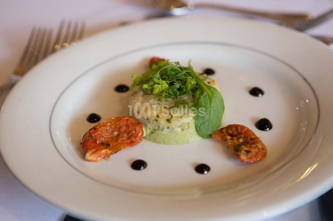 Plat gastronomique composé d'une mousse verte, de tomates confites, de sauce en points et de verdure en décoration.