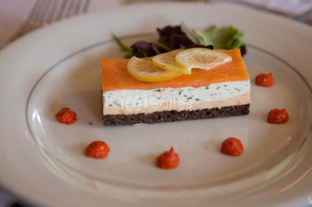 Entrée composée de saumon fumé, mousse aux herbes, pain noir, rondelles de citron et décorée de salade et sauce rouge.