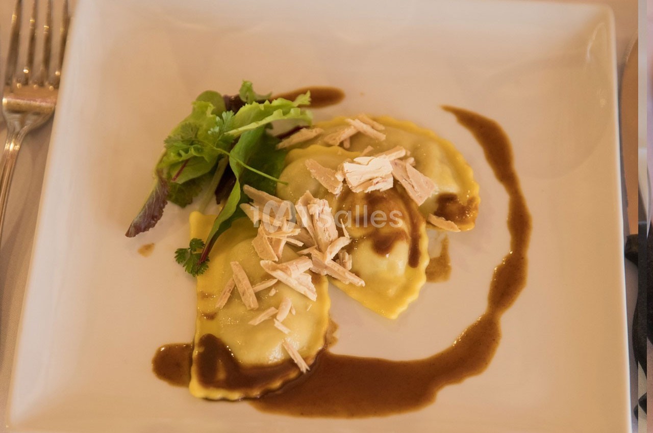 Assiette de raviolis garnis, nappés de sauce brune, accompagnés de copeaux et d'un bouquet de salade verte.