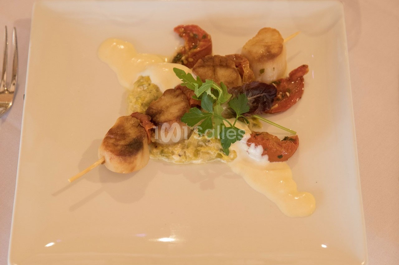 Brochette de noix de Saint-Jacques grillées servie avec une sauce crémeuse, tomates séchées et herbes fraîches.