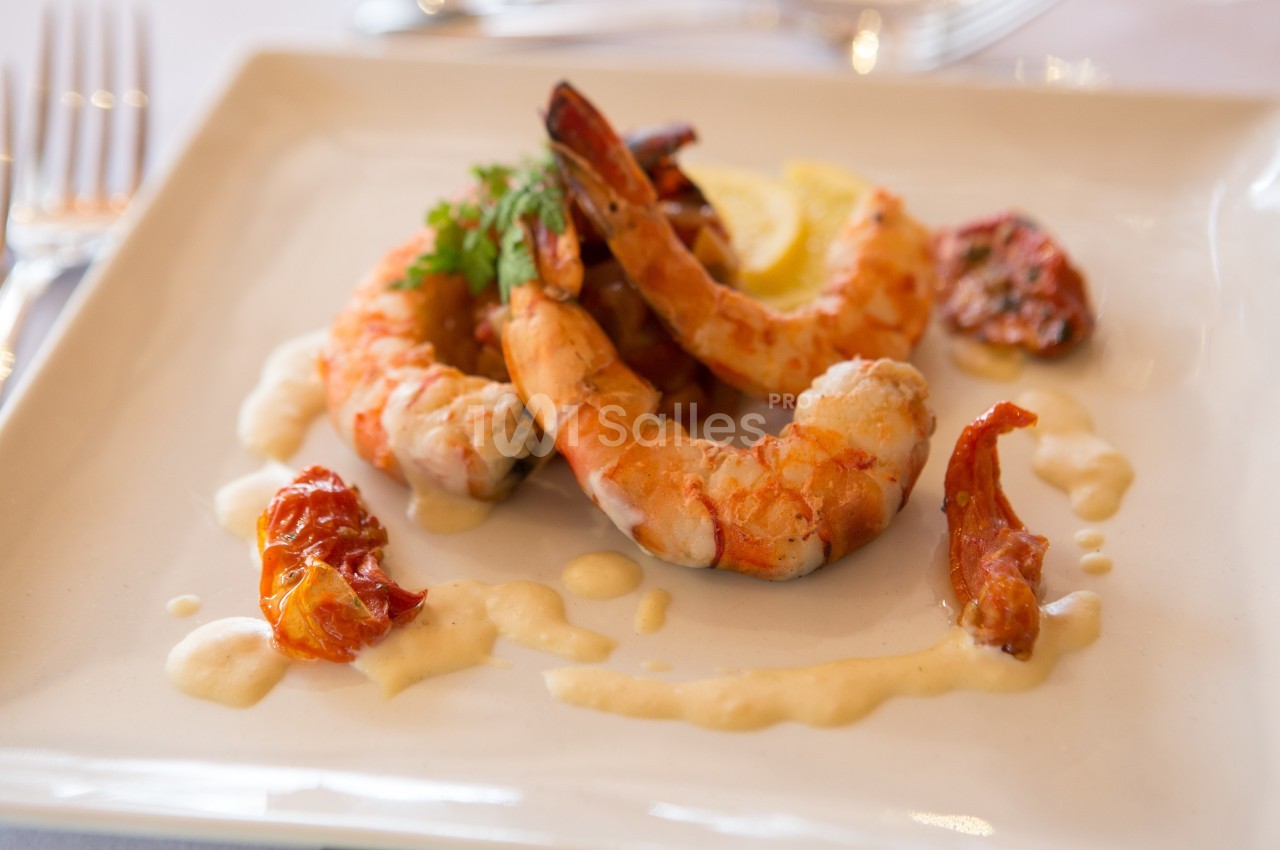 Assiette de crevettes grillées accompagnées de tomates séchées, d'une sauce crémeuse et d'une tranche de citron.