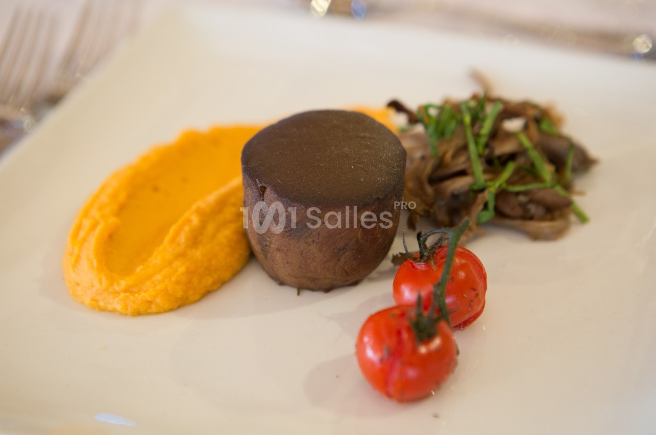 Assiette gastronomique avec purée orange, pièce de viande, champignons sautés et tomates cerises grillées.