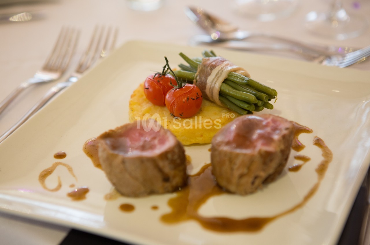 Assiette gastronomique avec filet de viande, haricots verts enroulés de lard, tomates cerises et purée, nappée de sauce.