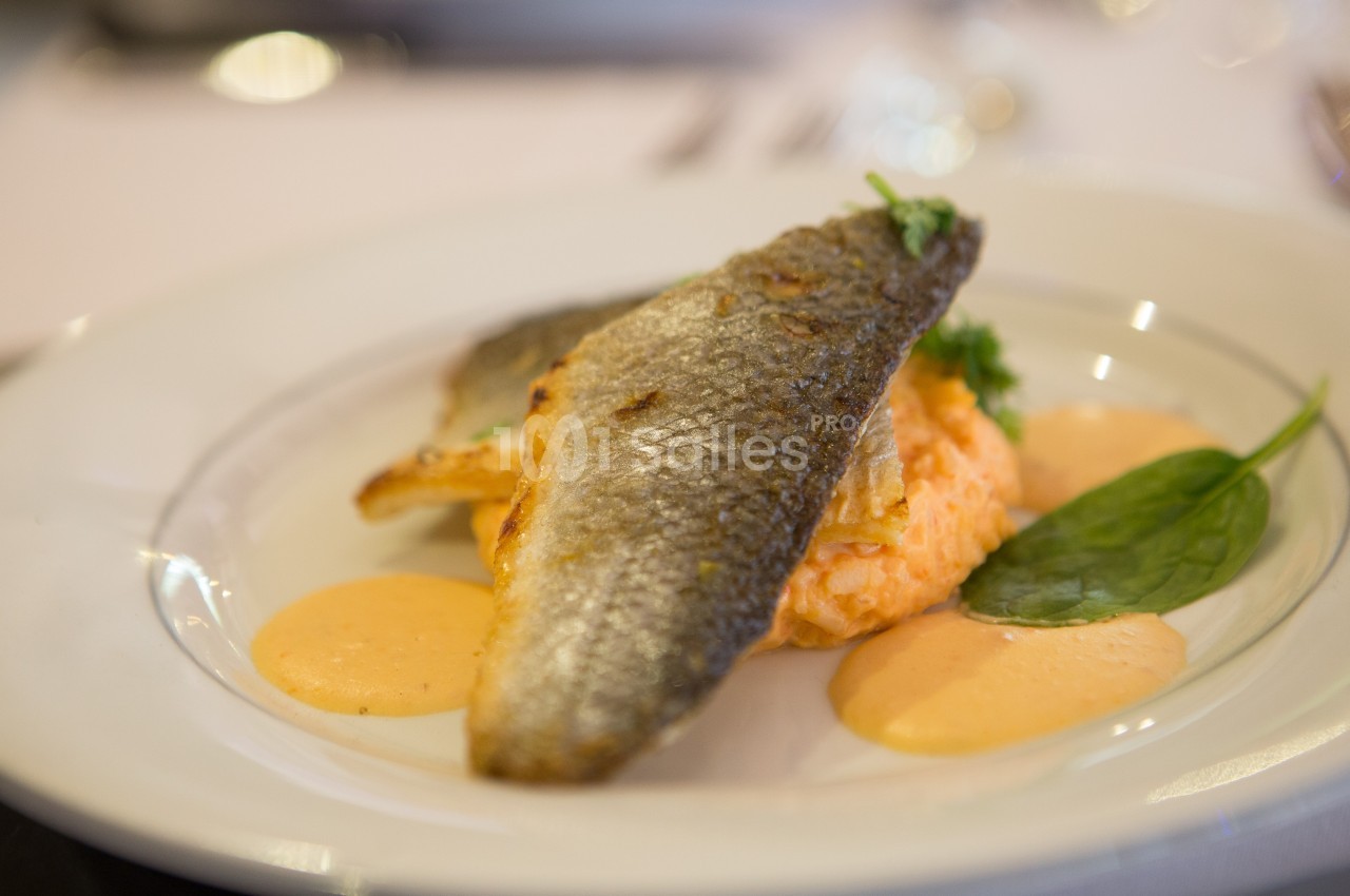 Filet de poisson grillé servi sur une purée orange avec des sauces et une feuille d'épinard en garniture.