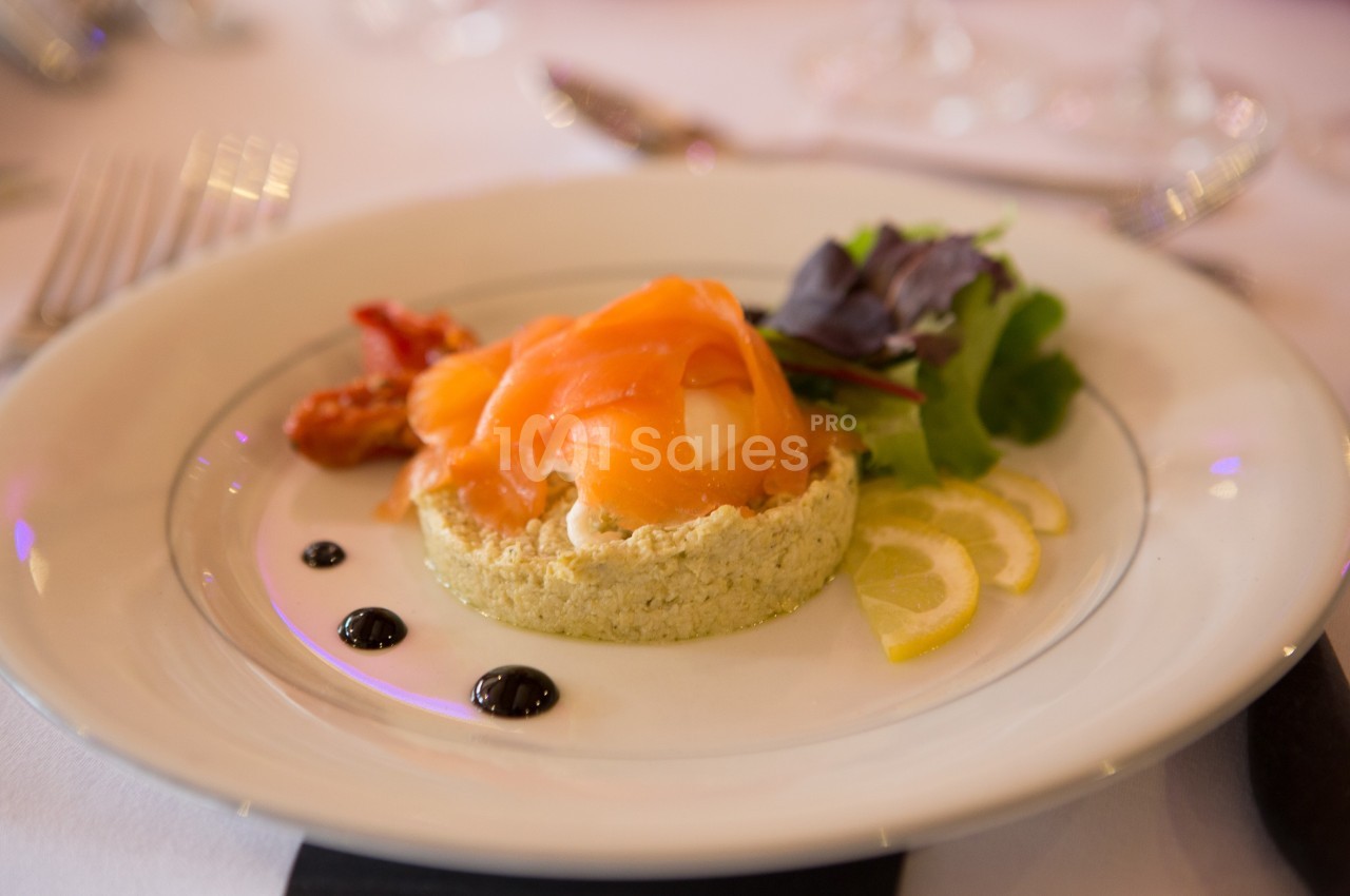 Assiette avec une entrée composée de saumon fumé, fromage frais, salade, rondelles de citron et sauce balsamique.